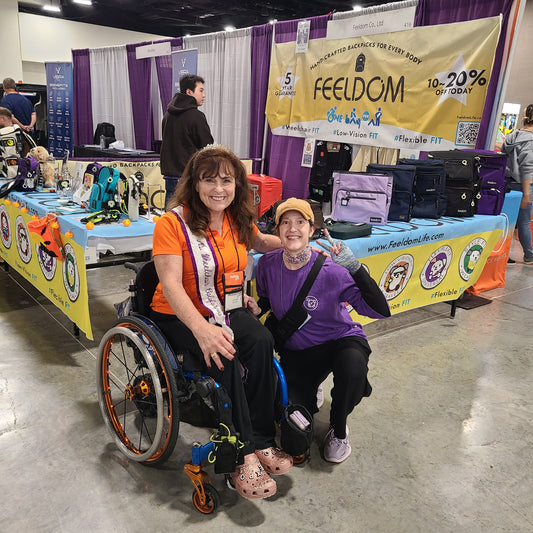 Adrianne and Ms. Wheelchair California, Julienne, wearing a sash and a sparkling tiara posing in front of the FEELDOM booth at the expo.