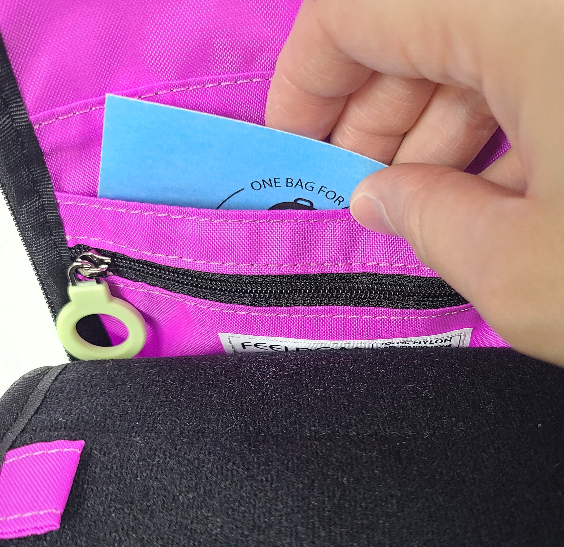 Close up detail of someone putting a 3 x 5 inch badge into the inner badge slot, so that the badge will show through the clear plastic window on the front.  The inner side of the badge slot is also a zipper pocket.